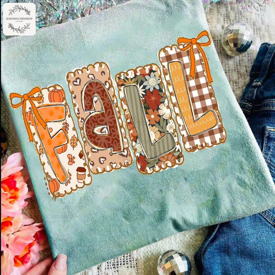 A light blue t-shirt with a festive FALL graphic design, shown with jeans and sparkly decorations for a coquette aesthetic.