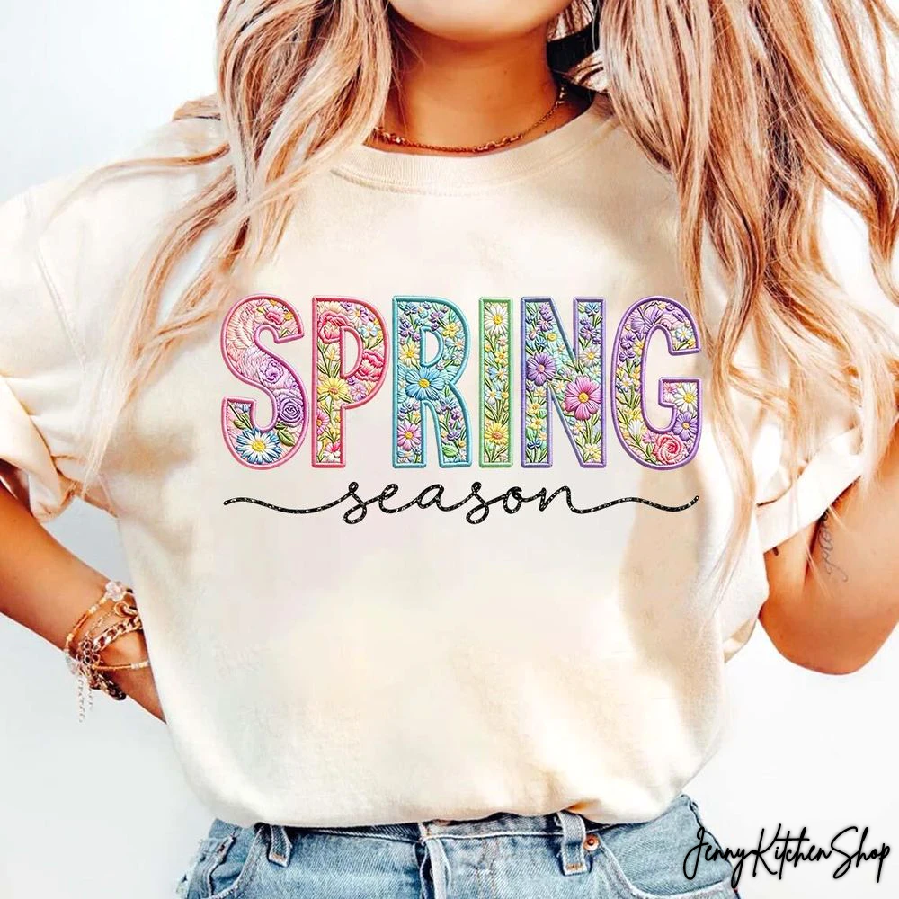 A woman models a cream-colored Easter Floral Varsity T-Shirt. The word SPRING has a colorful floral pattern.
